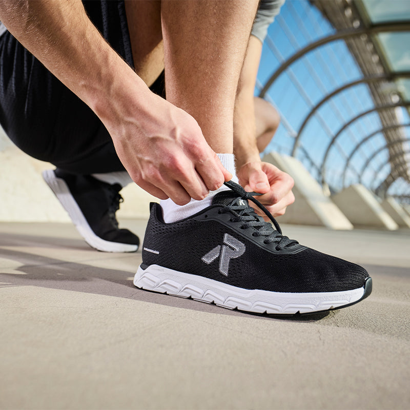 Men's black lace-up sneakers being tied, with cushioned white sole