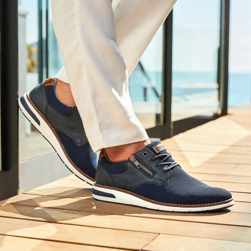 Men's navy mesh sneakers with tan collar trim, worn with light trousers