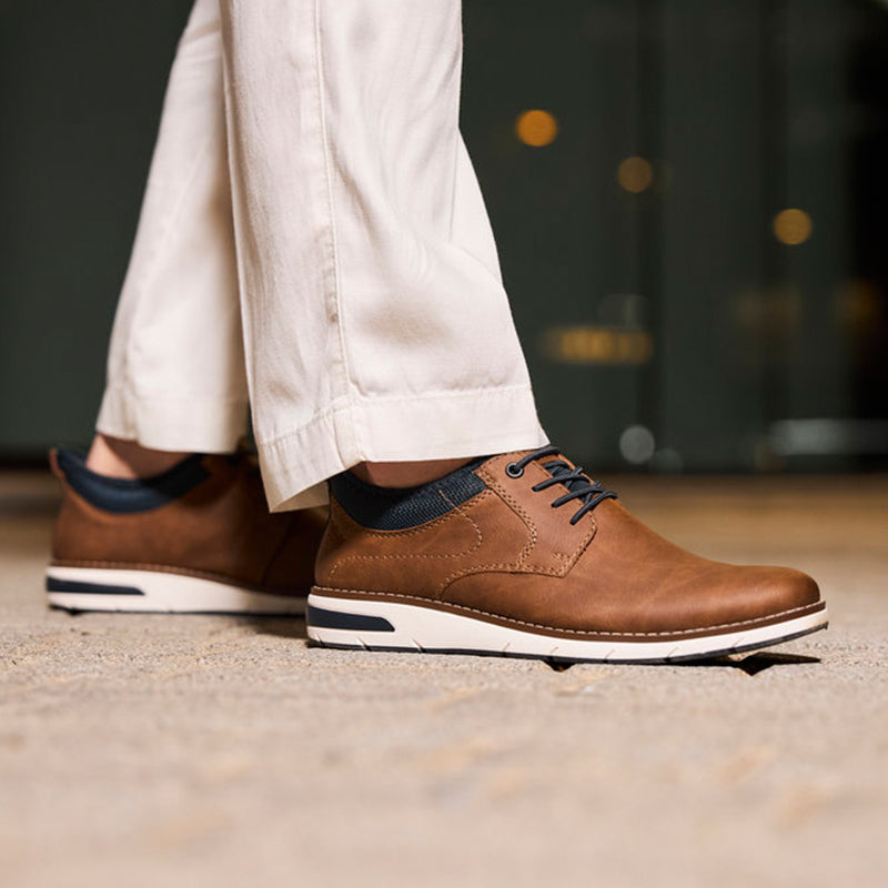 Men's brown lace-up sneakers with navy collar, worn with light pants