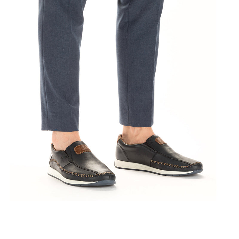 Men's blue leather slip-on loafers worn with dark trousers and white soles