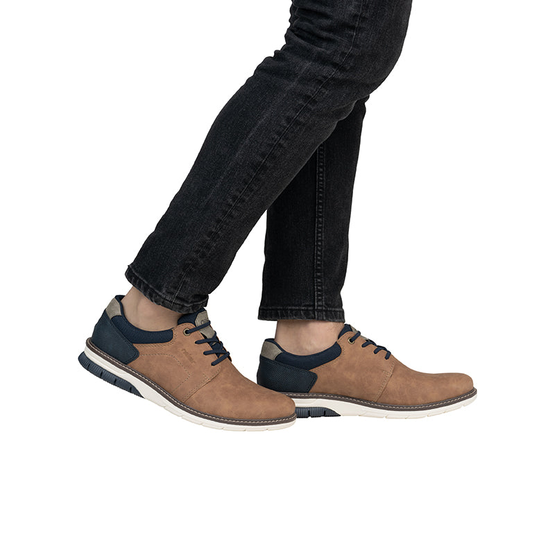 Men's lace-up sneakers on a person, chestnut suede with navy accents.