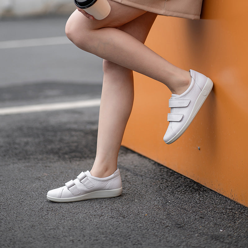 White leather sneakers worn with casual pants, two hook-and-loop straps and flat sole