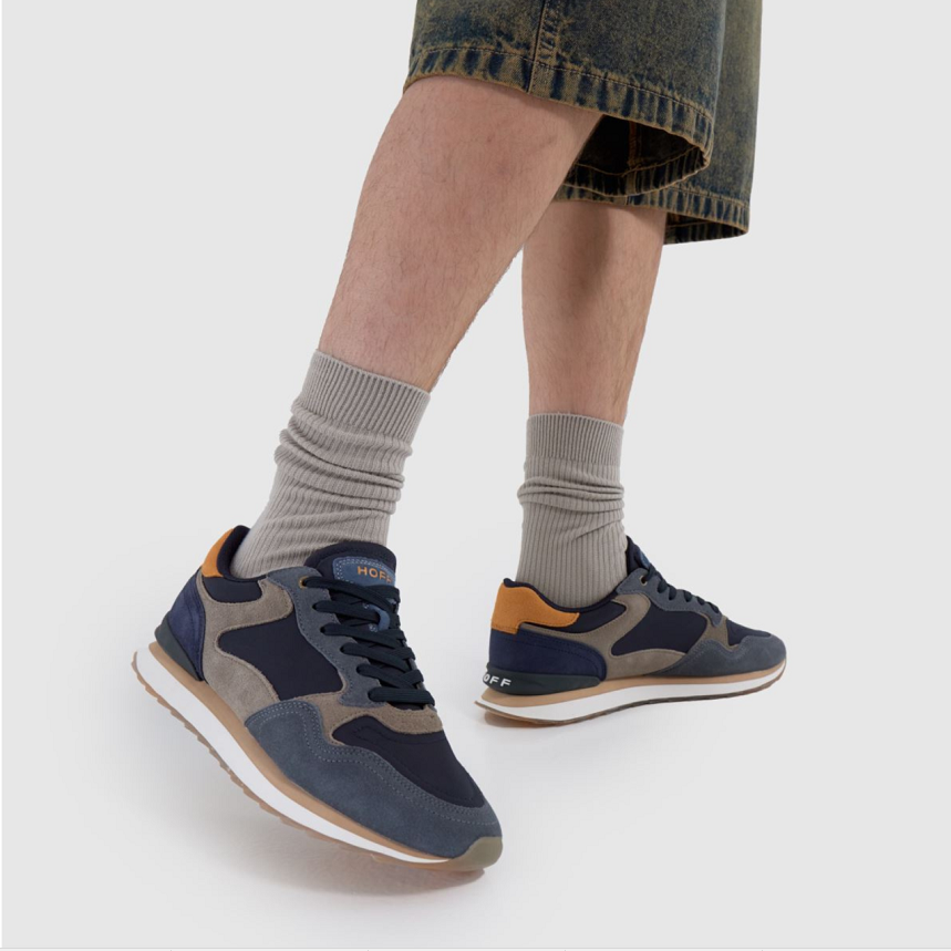 Men's sneakers with navy, tan, and gray panels, worn with gray crew socks