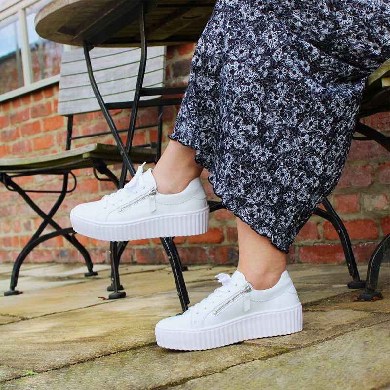 White leather platform sneakers worn with ankle socks and a dark floral dress