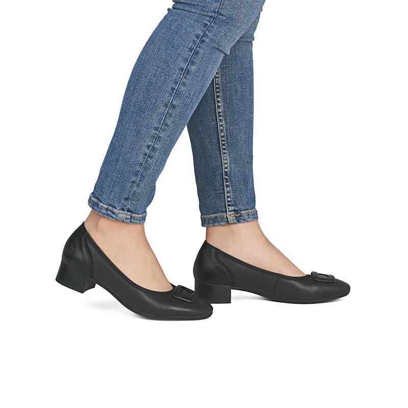 Black leather pumps on feet with low block heel and buckle strap, side view