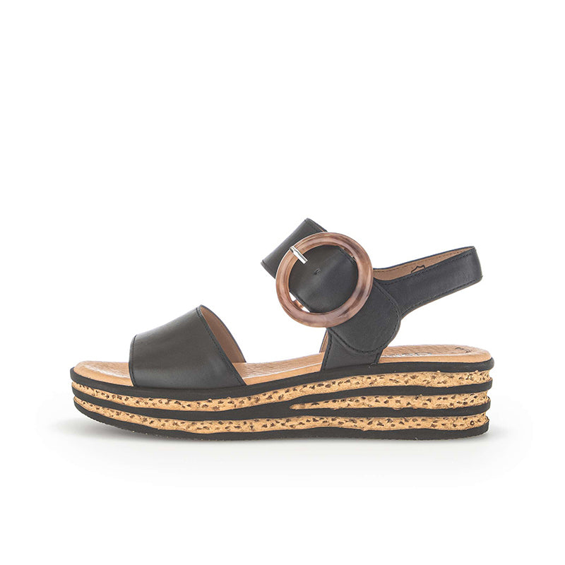 Women’s leather platform sandals in black, side view with round buckle detail and striped wedge sole