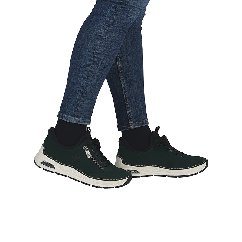 Dark green slip-on shoes with black collar and white sole worn with blue jeans