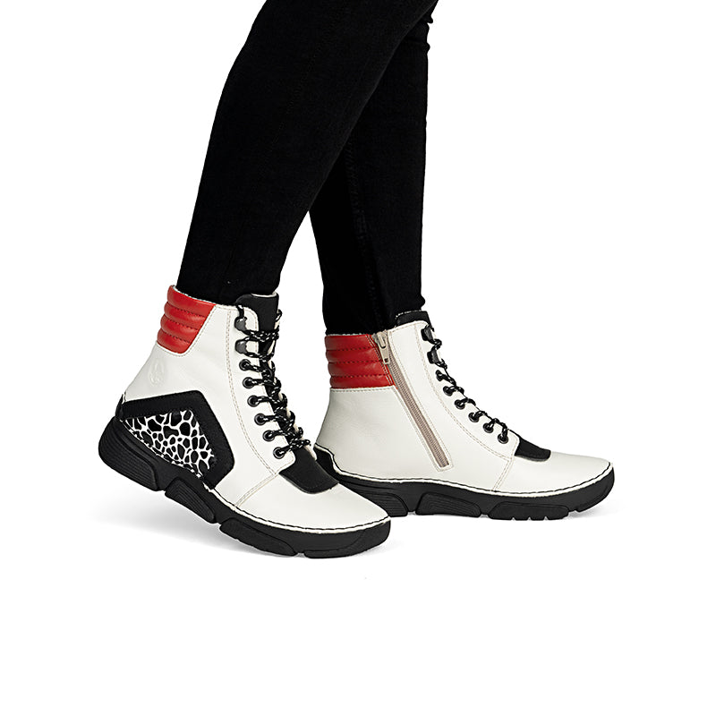 Women's lace-up ankle boots in white and black with red accents, worn with pants