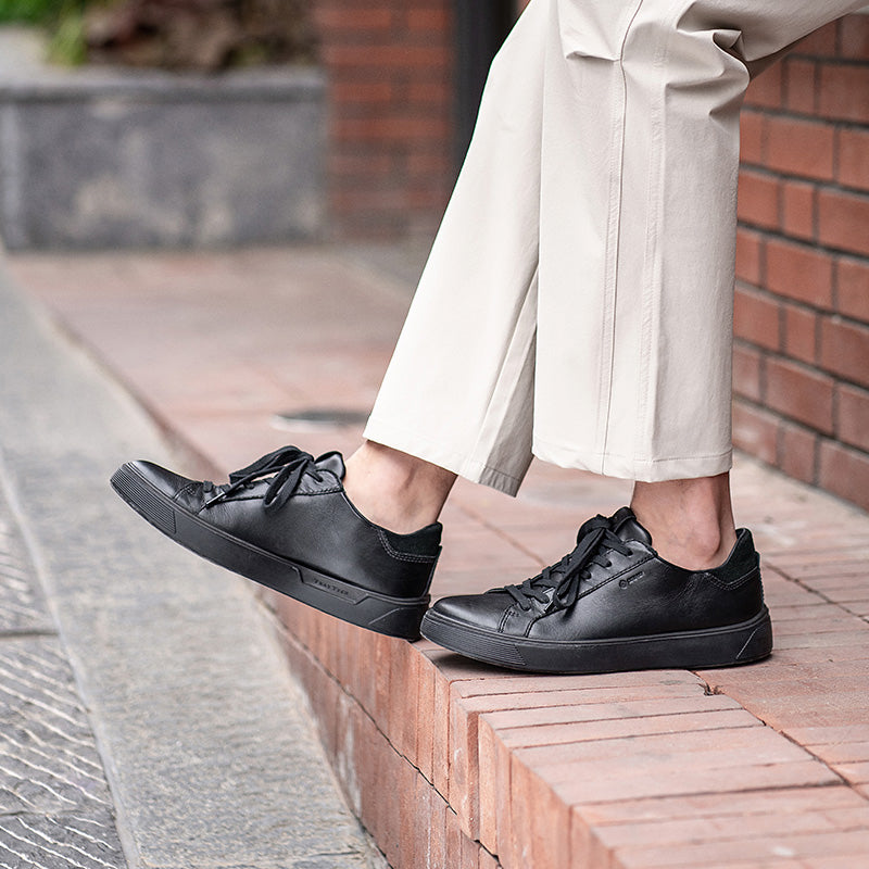 Black leather lace-up sneakers on feet with low rubber soles