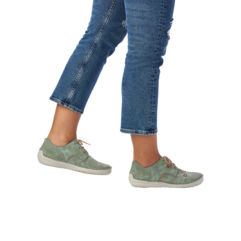 Green lace-up sneakers on model feet with white rubber sole