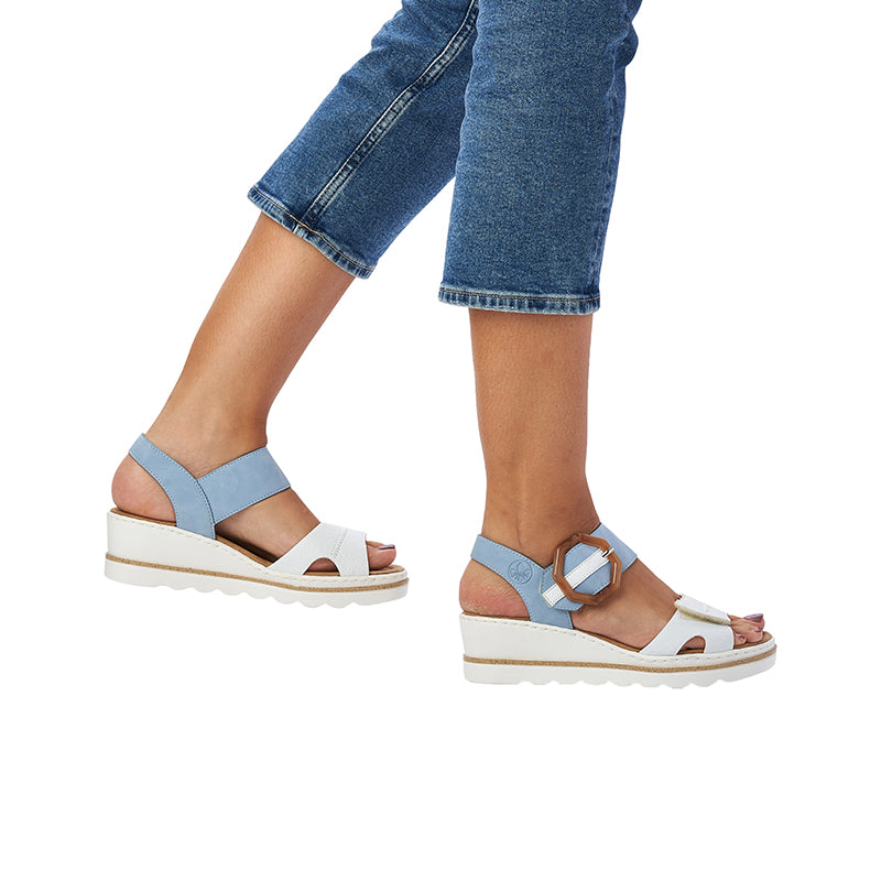 Light blue and white wedge sandals on feet with tan buckle accent