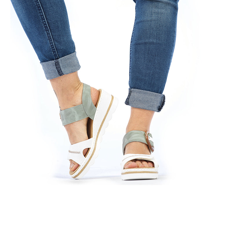 Wedge sandals on feet with light green straps and white sole, worn with jeans