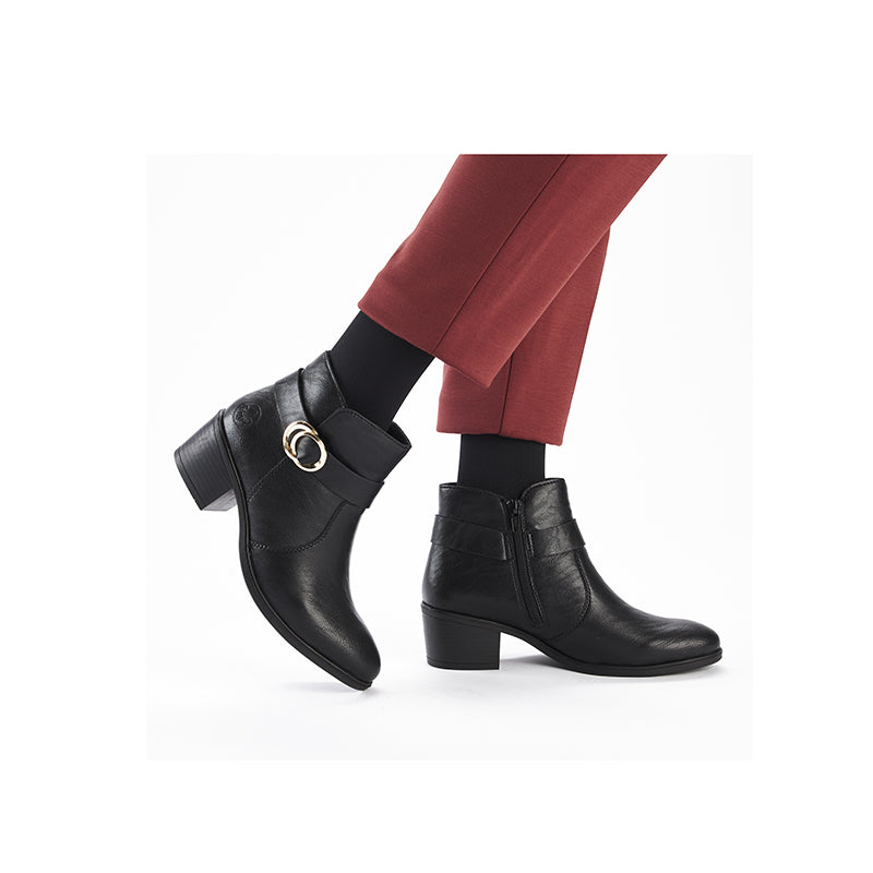 Black leather ankle boots with buckle strap and block heel, worn with pants