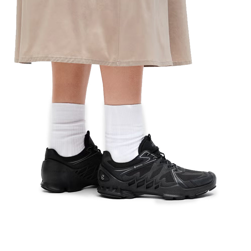 Black waterproof lace-up sneakers with white socks and cropped pants, treaded outsole