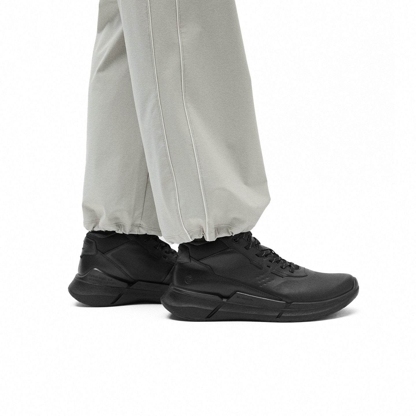 Men's black lace-up sneakers with thick sole, worn under light pant cuffs