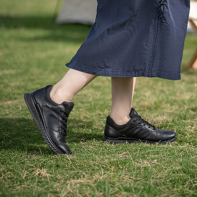 Black leather sneakers worn with a dark skirt hem