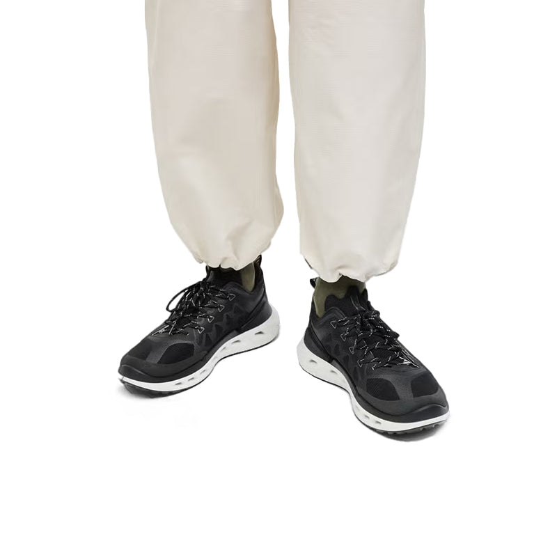 Black men's sneakers on feet with light pants, white outsoles visible