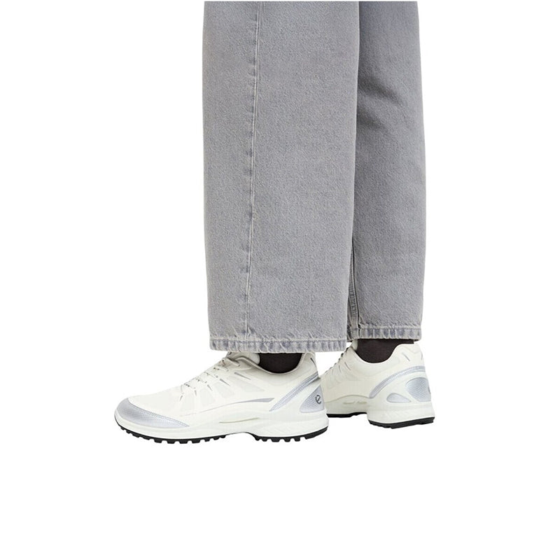 Men's white sneakers worn with light gray pants cuffs and lace-up front