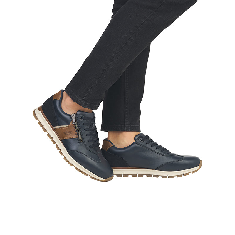 Men's lace-up sneakers with navy upper and tan side zipper, worn with jeans.