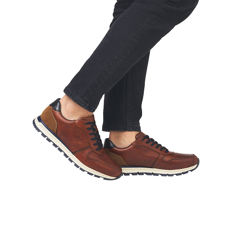 Men's brown lace-up sneakers on feet with dark pants and contrast white sole