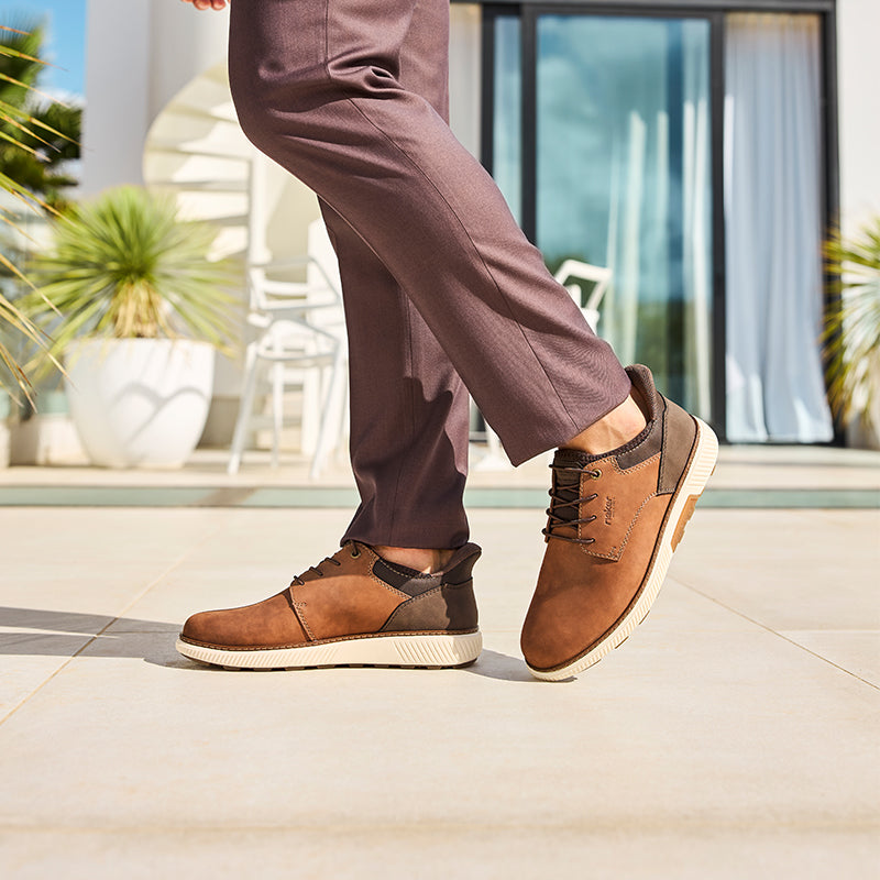 Men's brown lace-up sneakers with dark pants and low-profile sole