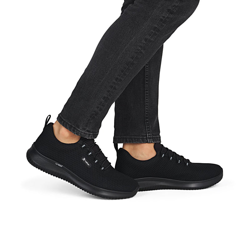 Men's slip-on sneakers in black with lace-up front and dark rubber sole; on feet with jeans