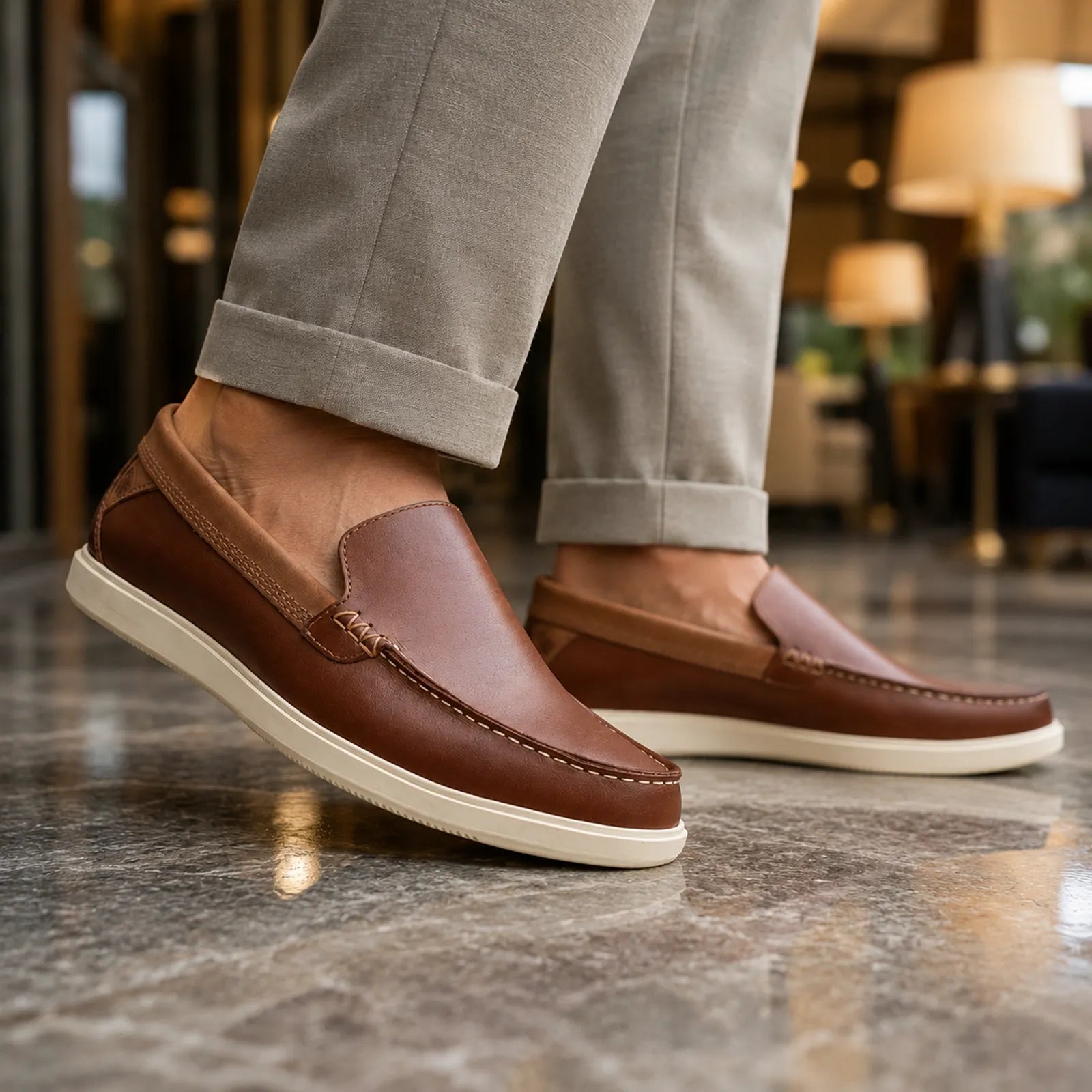 Men's brown slip-on loafer shoes with white sole, worn with gray pants