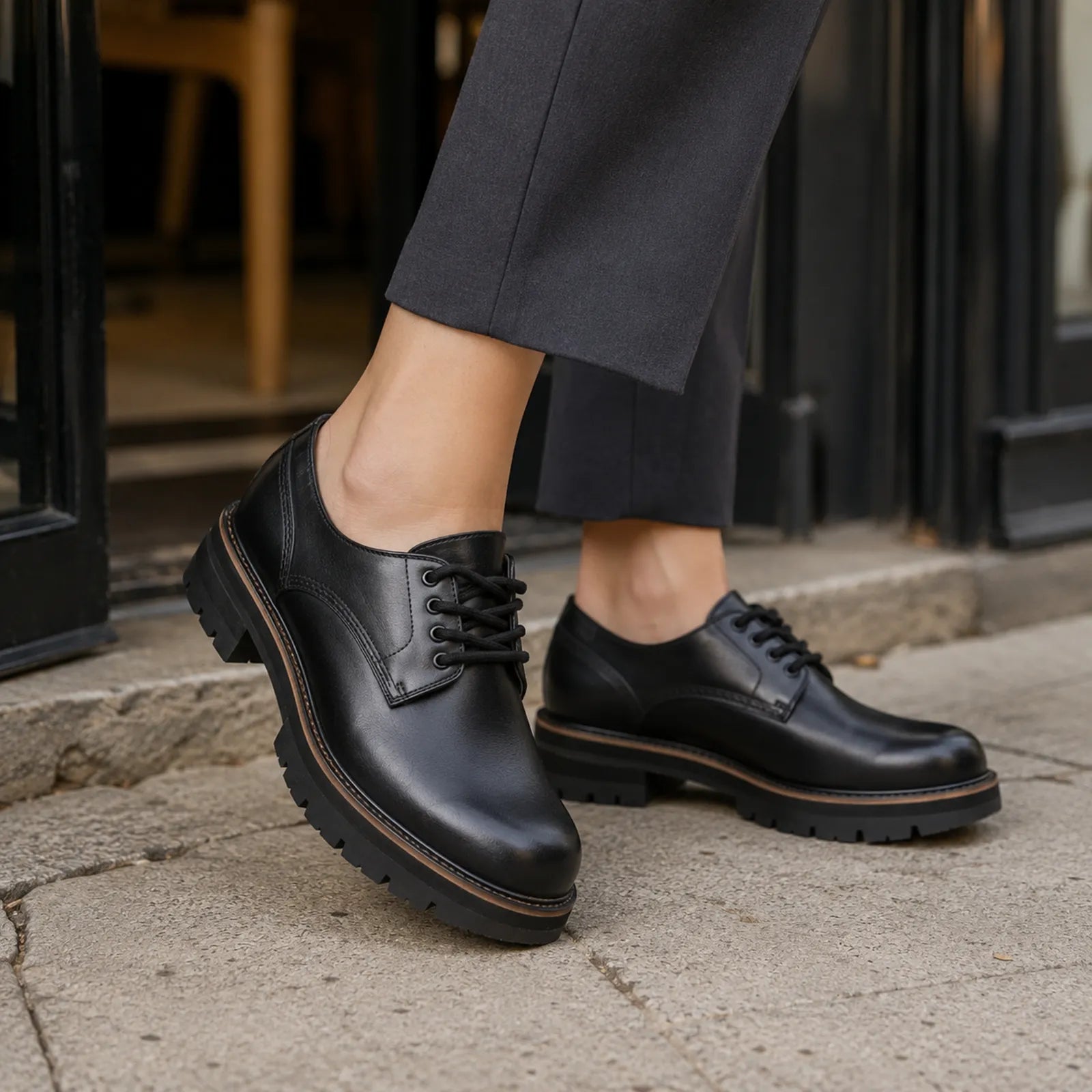 Black leather lace-up derby shoes with thick tread sole and rounded toe.