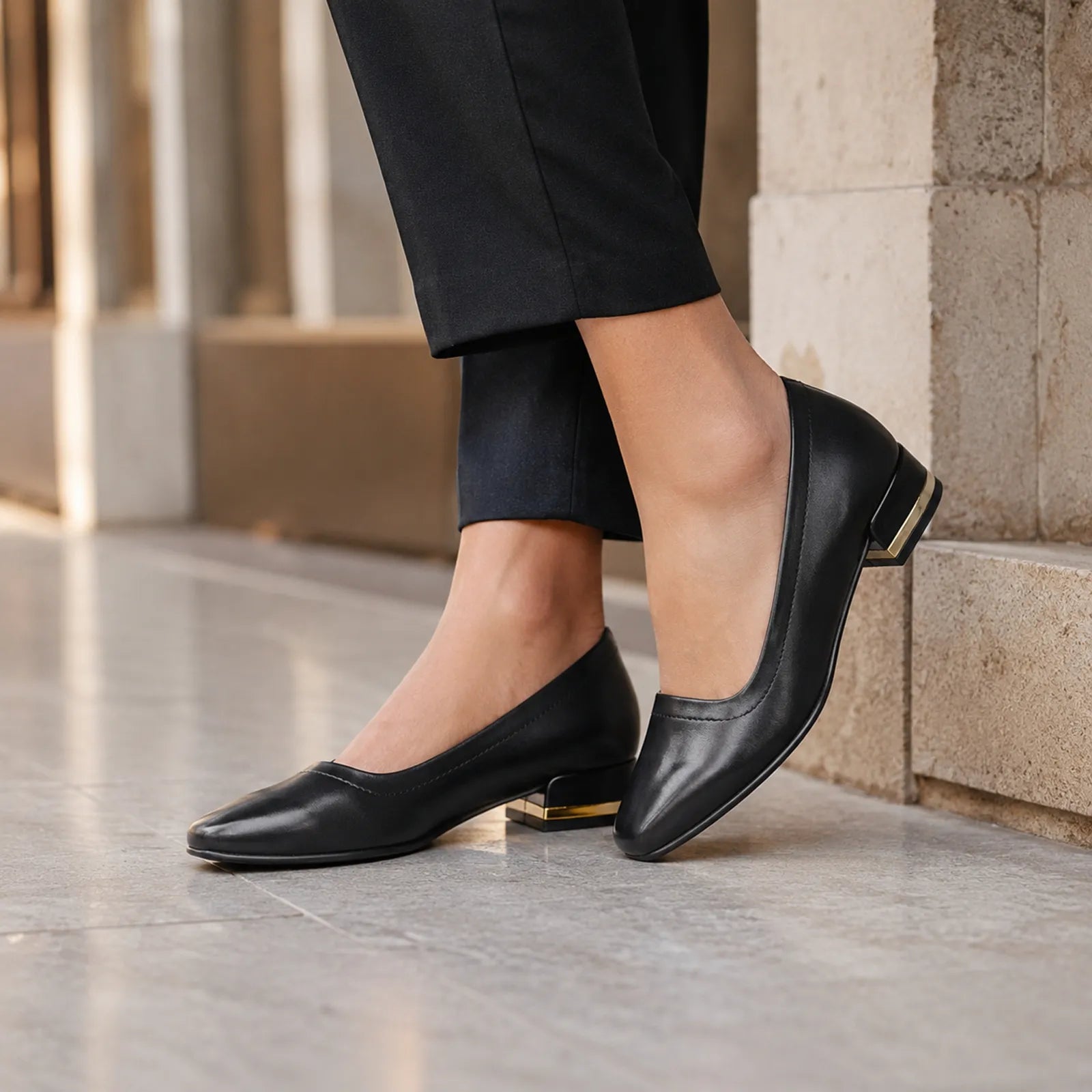 Black women's court pumps on feet, rounded toe and low block heel with gold accent