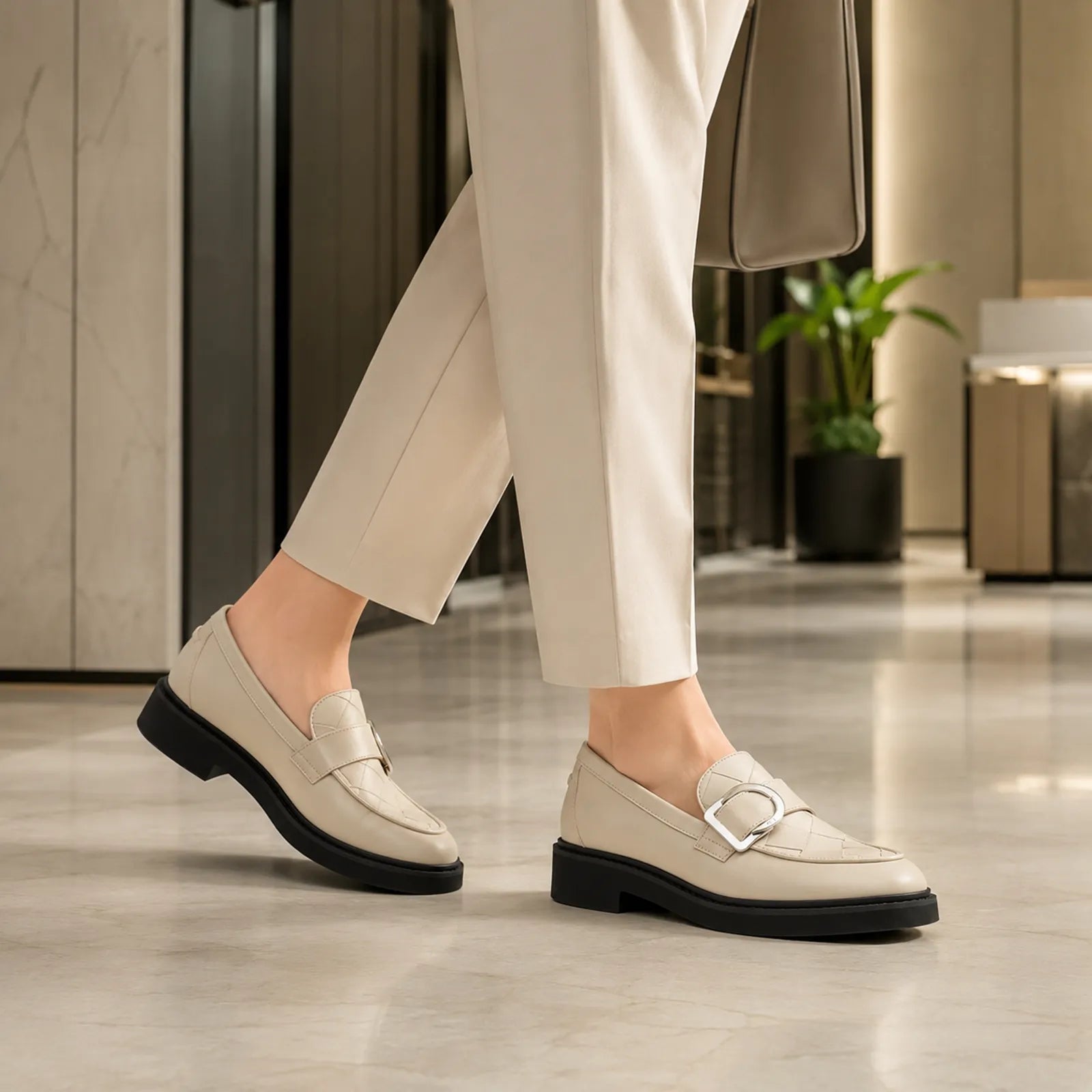 Beige penny loafers with metal buckle and chunky black sole under ankle-length pants