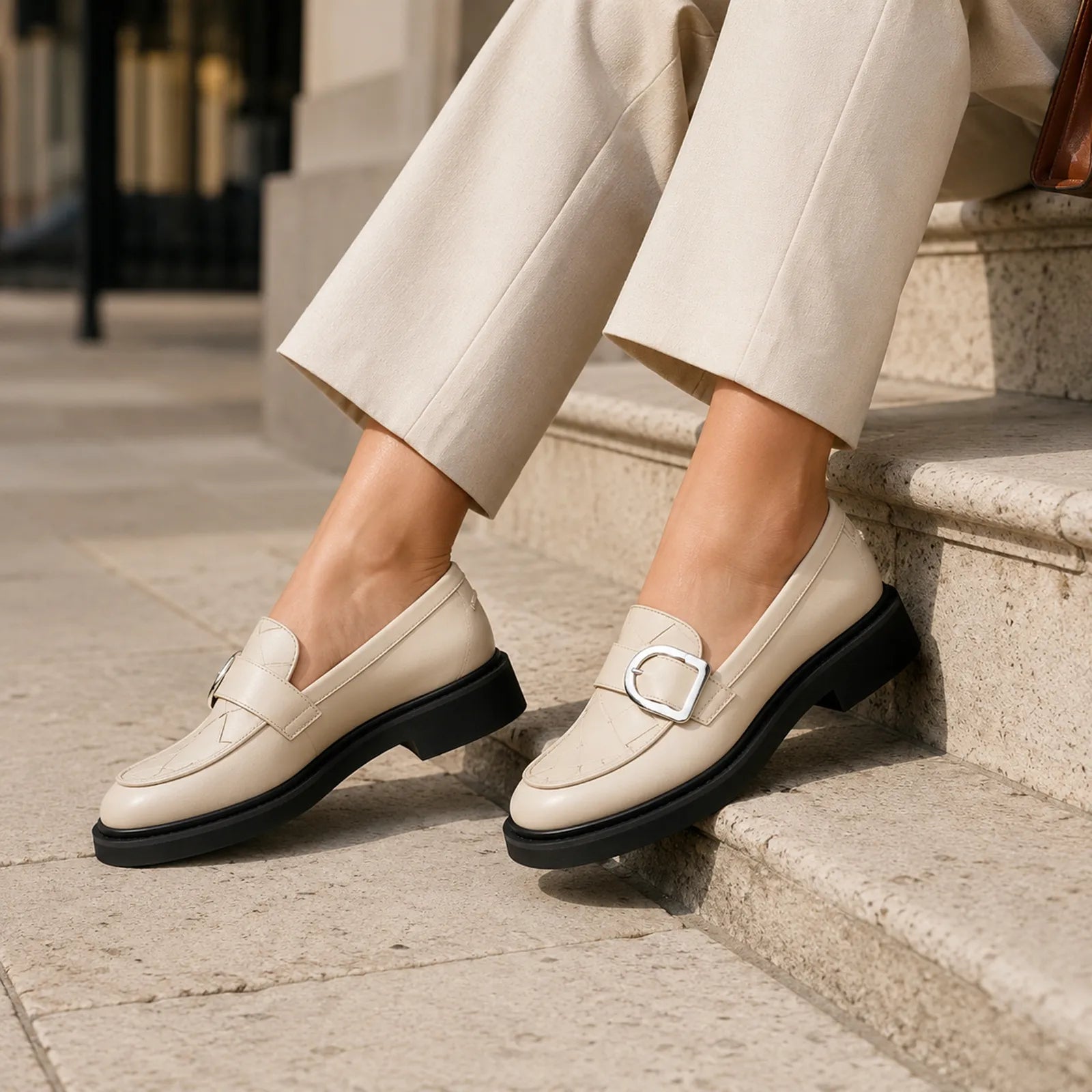 Beige penny loafers with metal buckle and thick black outsole worn with cropped pants