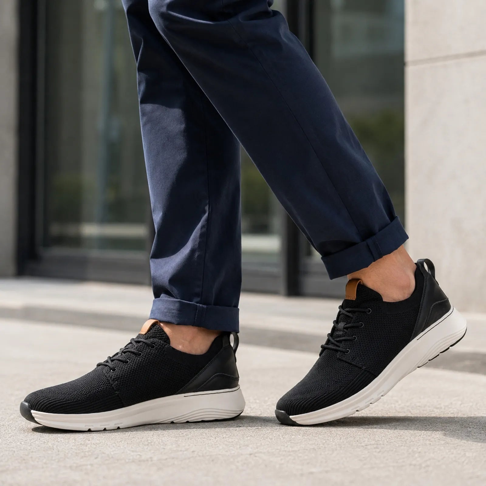 Men's black knit lace-up sneakers on pavement with white sole and tan heel pull