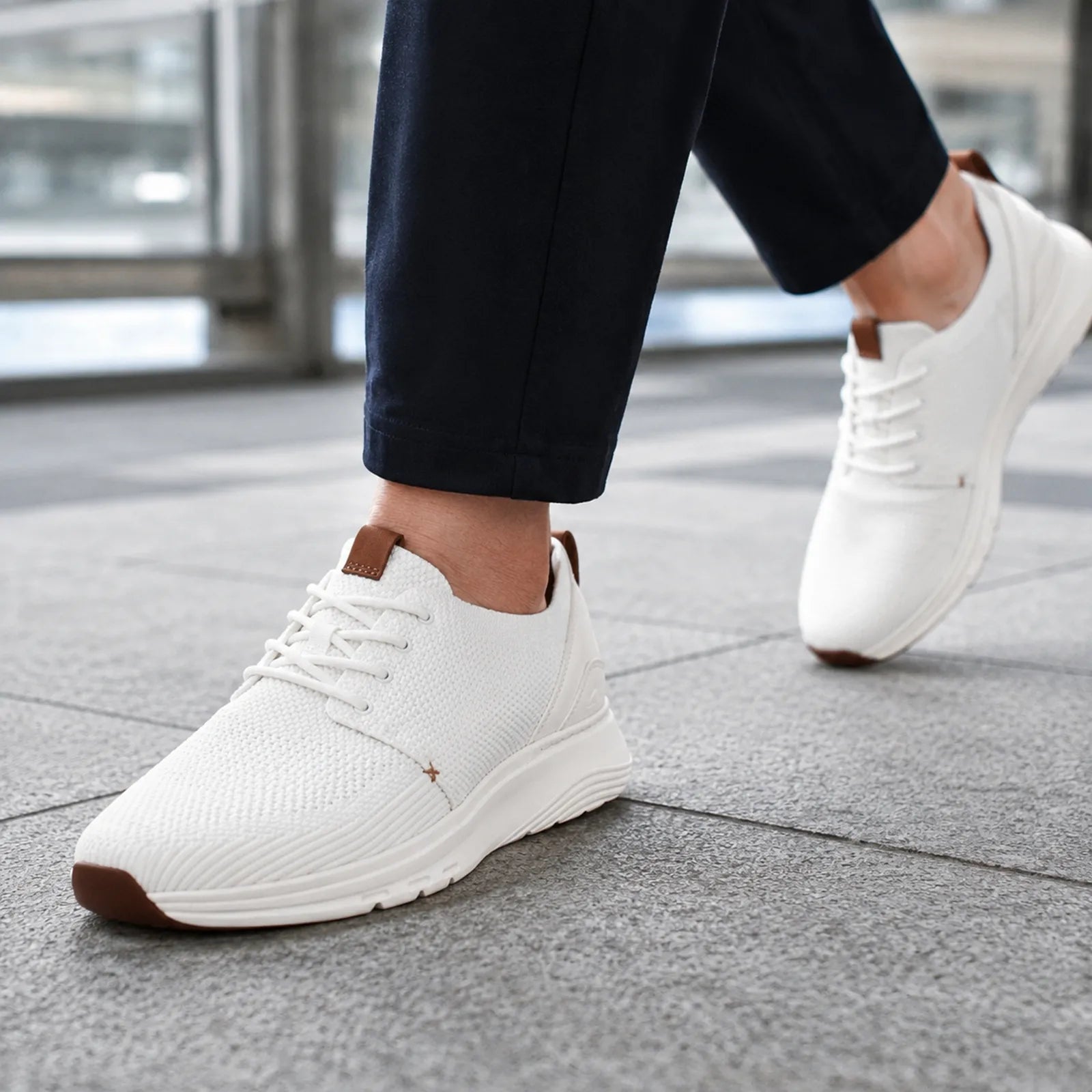Men's white lace-up walking sneakers worn with black pants; brown heel tab and white sole