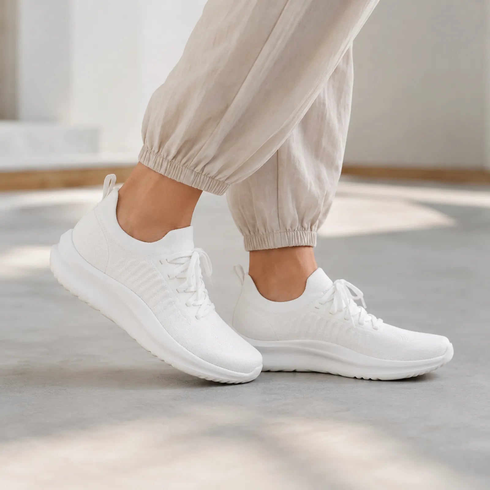 White lace-up sneakers on a person, knit upper and cushioned sole