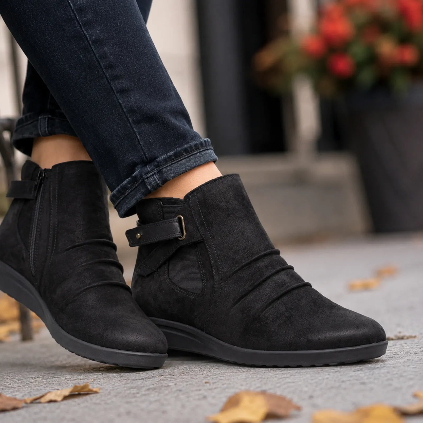 Women’s black suede mid boots with buckle strap on textured outdoor pavement