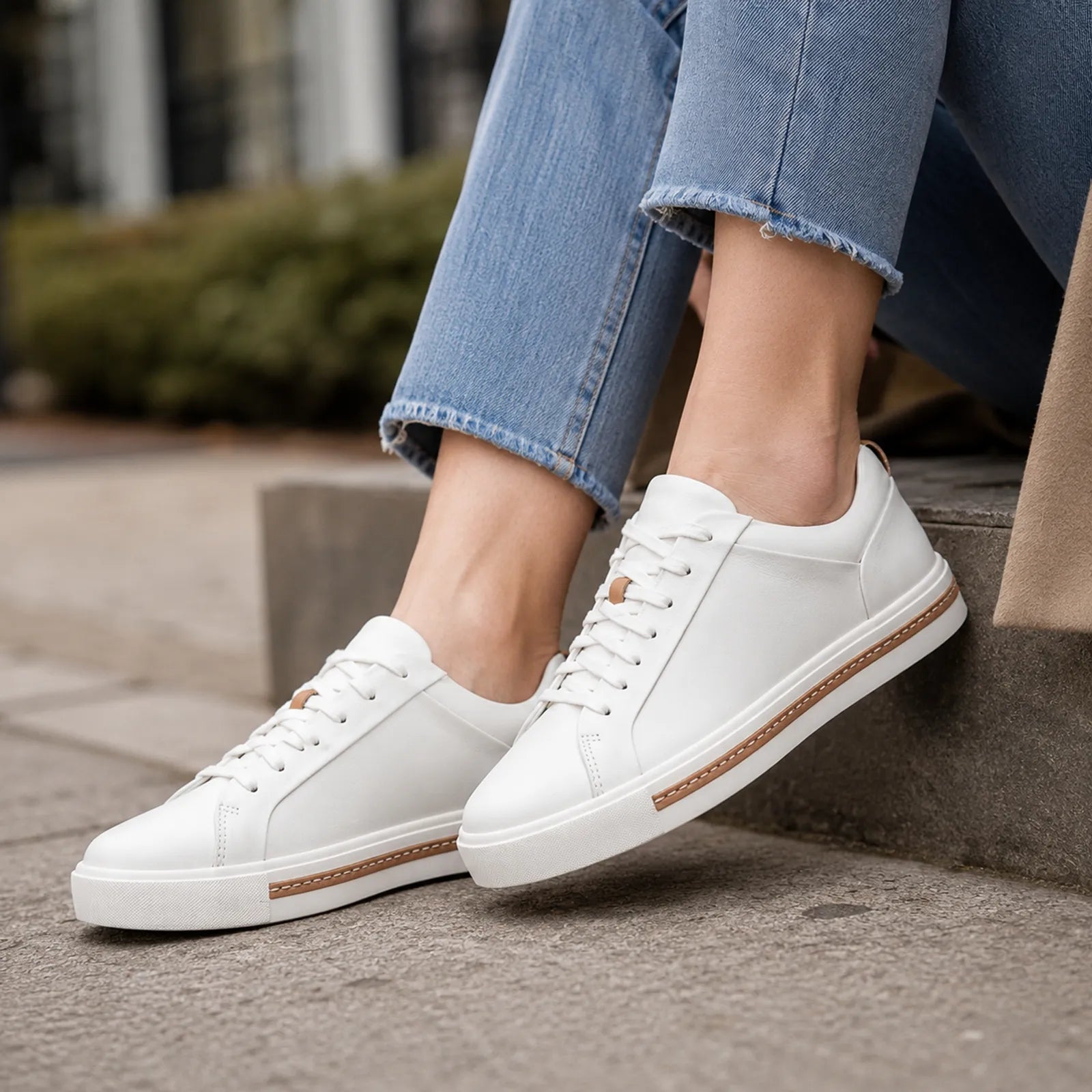 White leather low-top lace-up sneakers with tan side stripe, shown with cropped denim