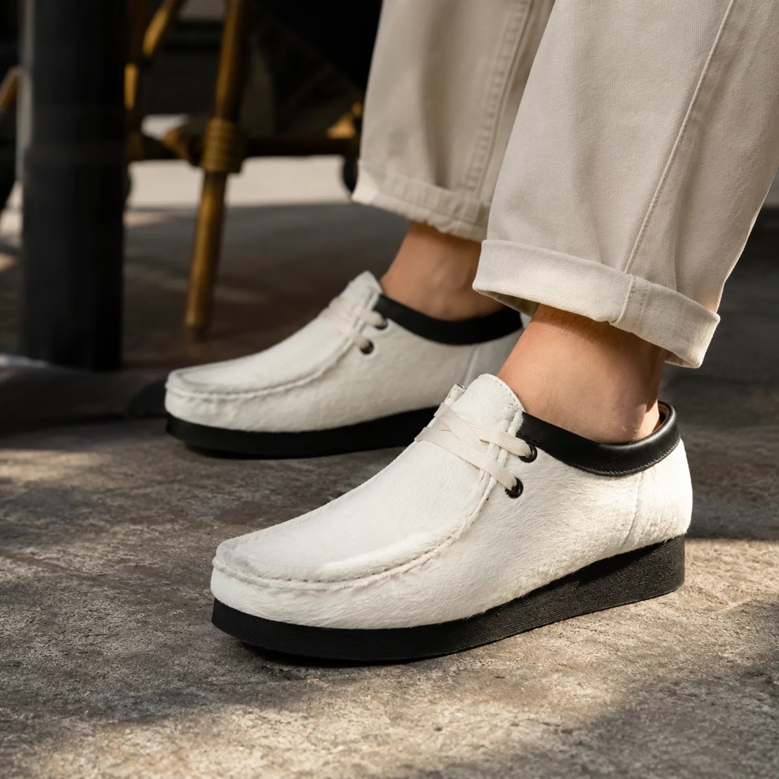 Close-up: white Wallabee-style lace-up shoes with black collar and thick sole