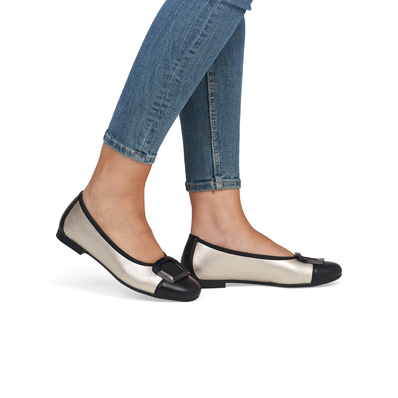Women's cream and black flat pumps worn with denim pants, rounded toe