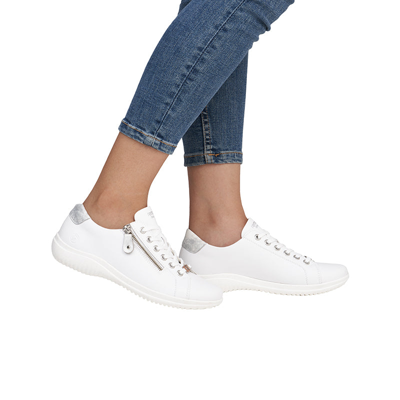 White low-top sneakers with lace-up front, worn with blue jeans