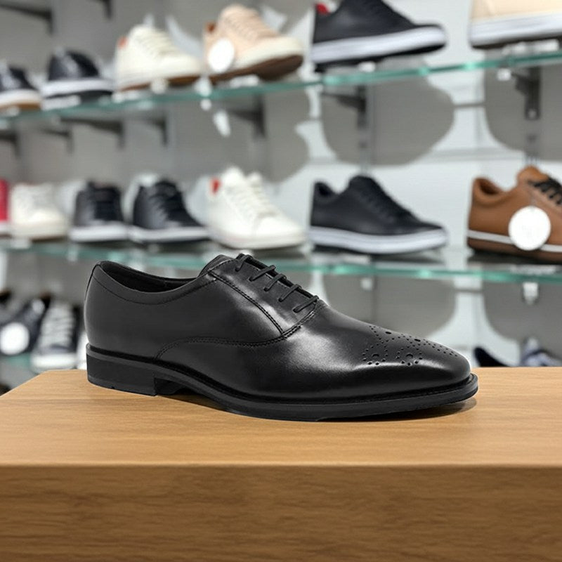 Black leather oxford dress shoe on wooden surface, lace-up with perforated toe
