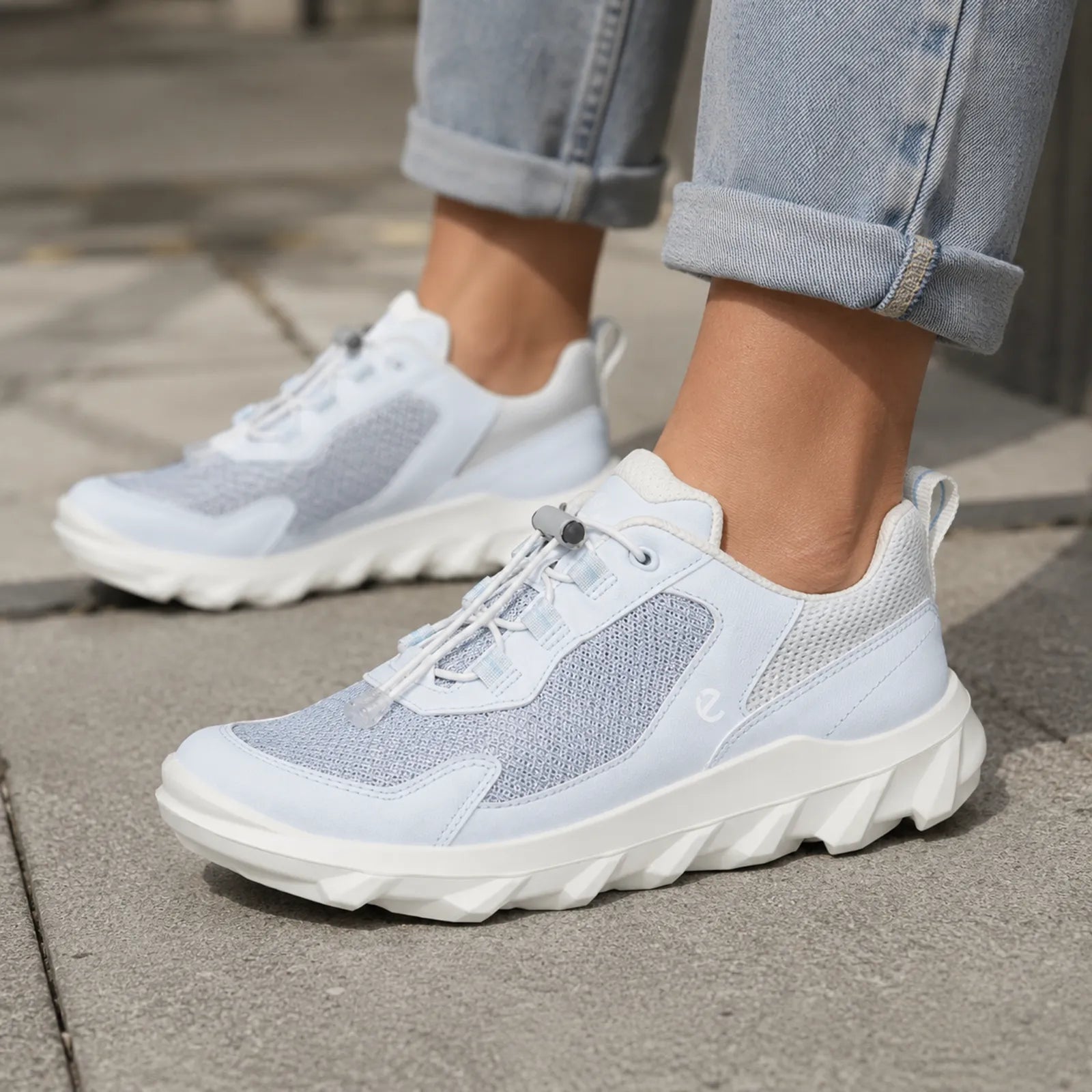 White and light blue lace-up women's sneaker worn with rolled jeans on pavement