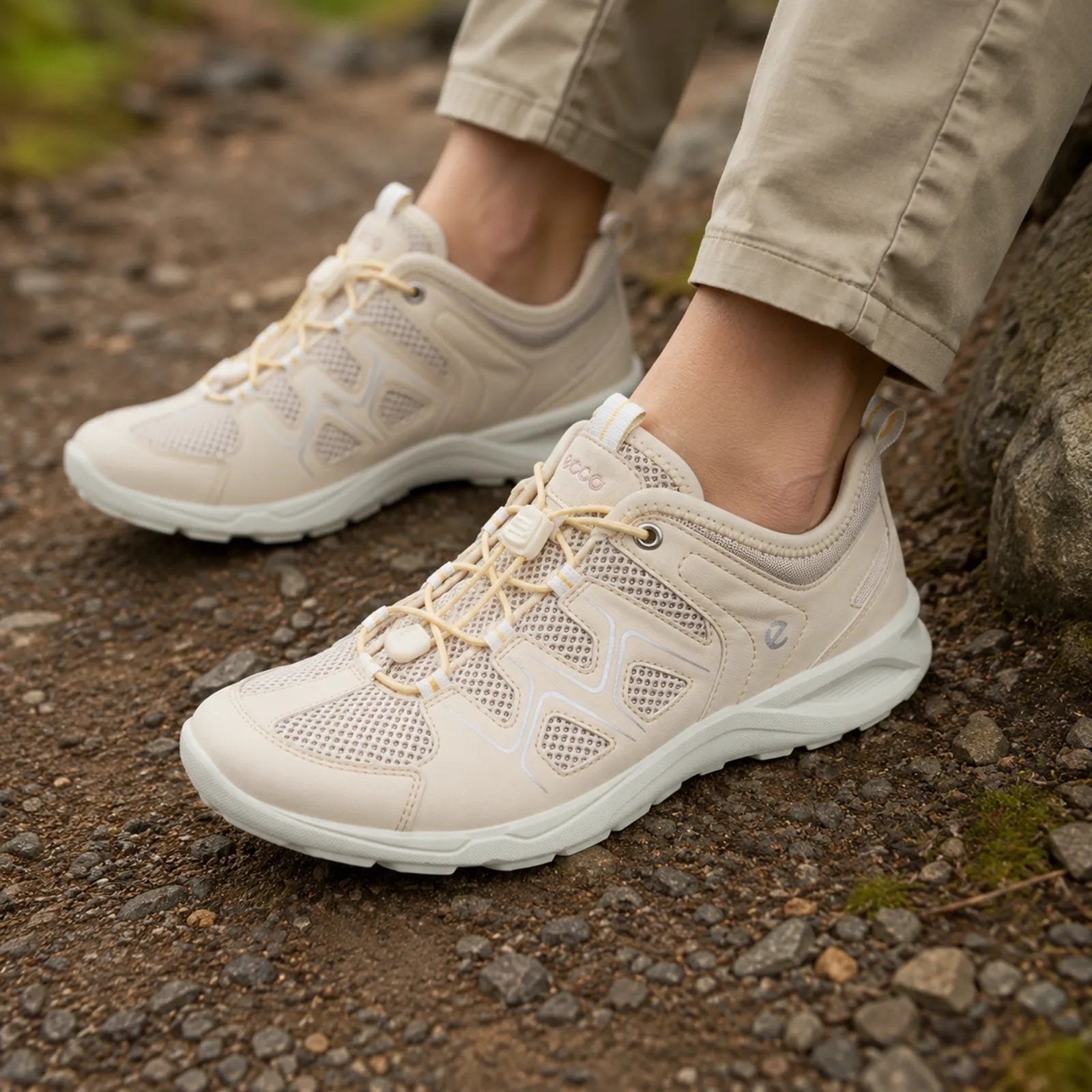 Women’s beige trail sneakers with lace-up closure and white midsole on rocky ground