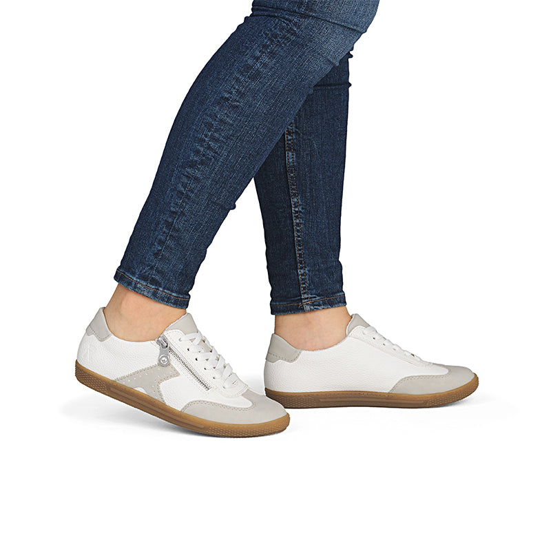 White low-top sneakers with lace-up and side zip, worn with blue jeans