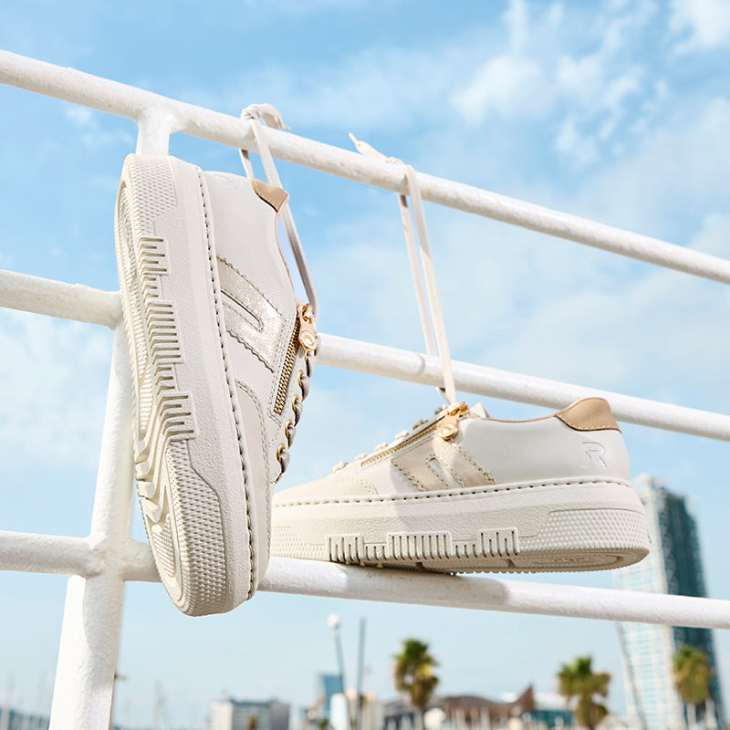 White lace-up trainers with gold zipper detail, hanging on display hooks