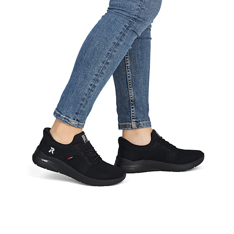 Pair of women’s black lace-up sneakers on feet with thick tread sole