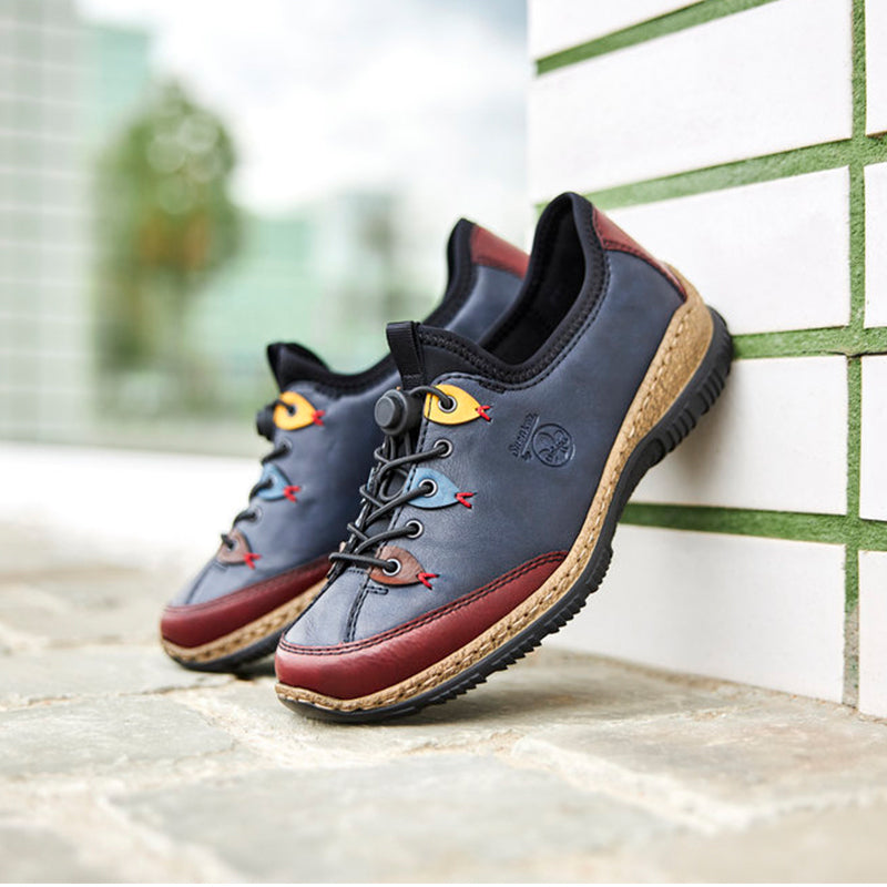 Women’s slip-on sneakers leaning by wall, dark blue upper with red trim and lace detail
