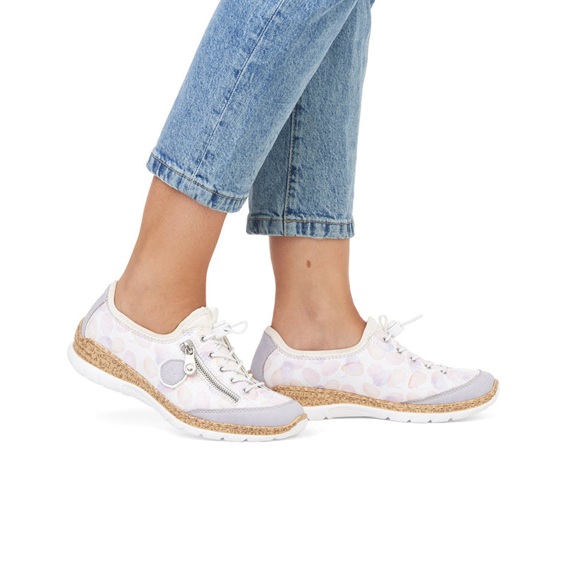 Women's sneakers worn with light blue jeans; white/pastel pattern and tan sole
