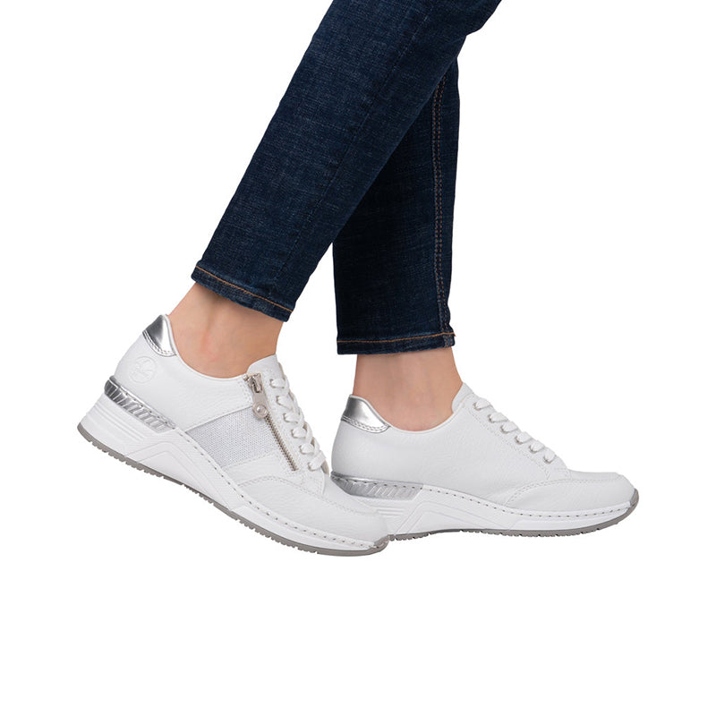 White leather sneakers with lace-up and side zipper, worn with blue jeans.