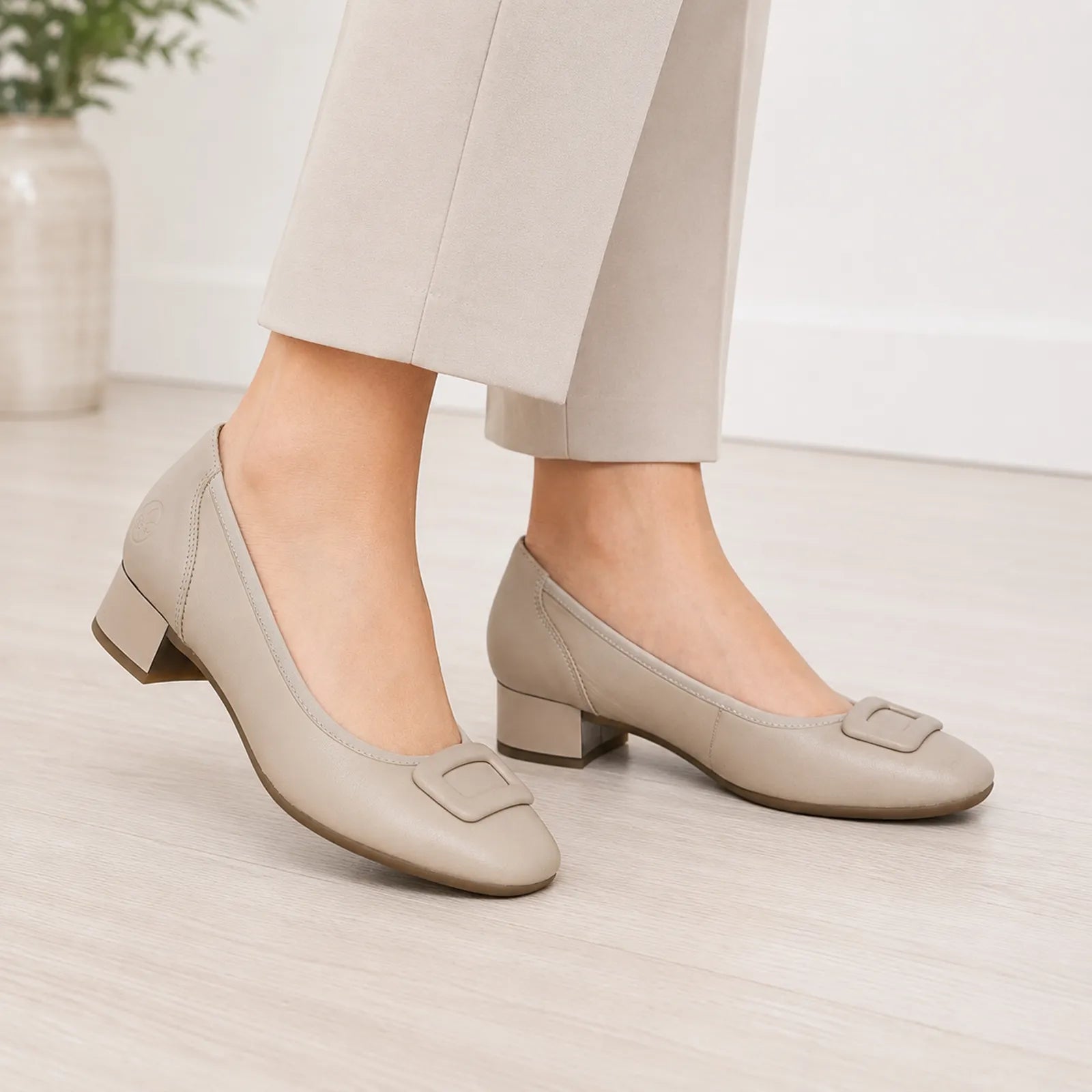 Beige leather pumps on feet with low block heel and buckle strap
