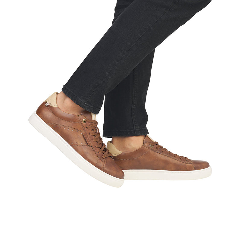 Brown lace-up sneakers on foot with dark jeans and white rubber sole